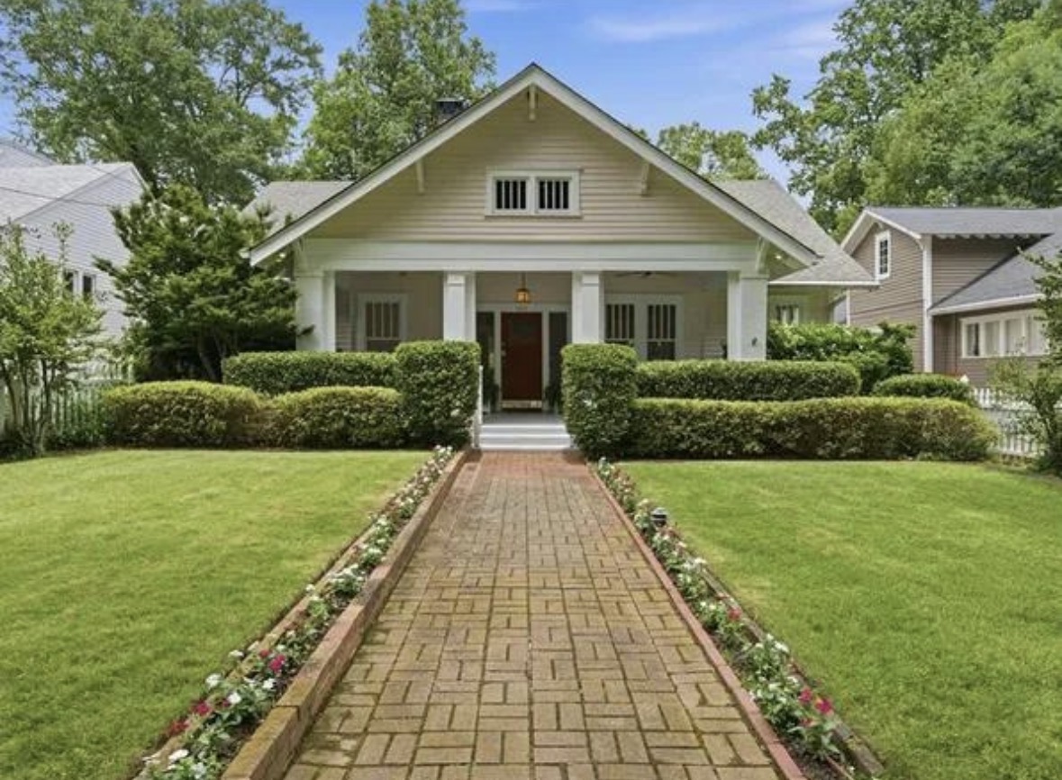 A centered bungalow with a covered front porch, brick walkway and green lawn